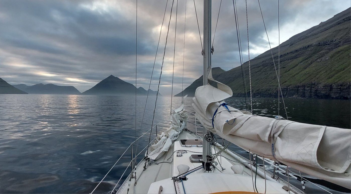De Stern vaart een fjord in onder een dreigende wolkenlucht, met steile rotswanden aan beide kanten